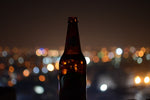 Brown glass bottle of root beer with background view of city skyline at dusk