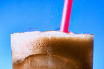 Fizzy cola beverage in glass with red plastic straw