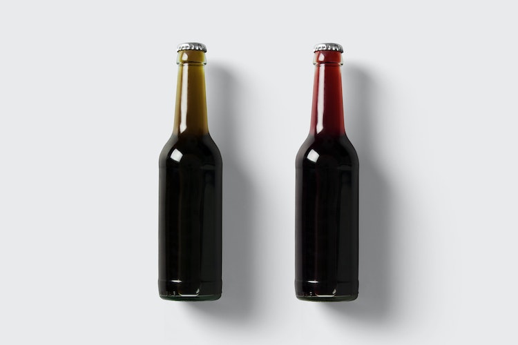 Two unopened glass soda bottles with white lids and different flavors